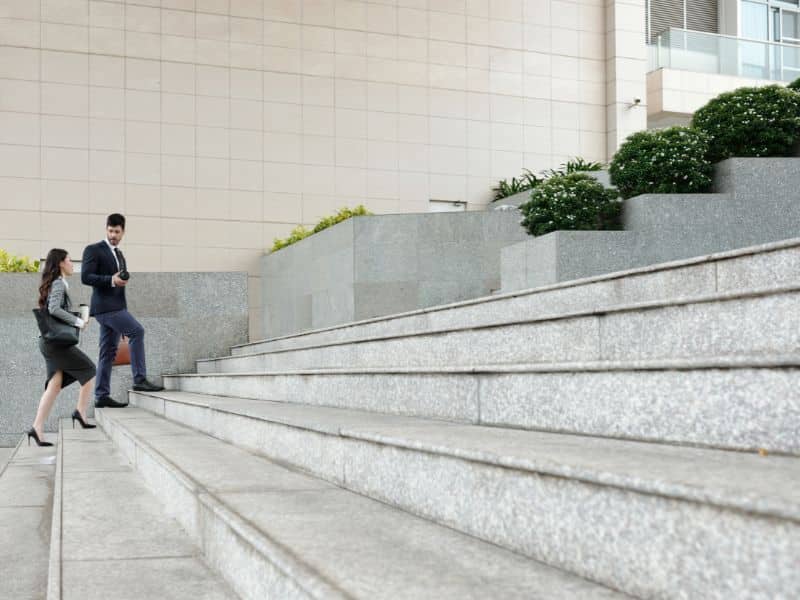 "Two business professionals walking up a wide set of outdoor steps while talking.
