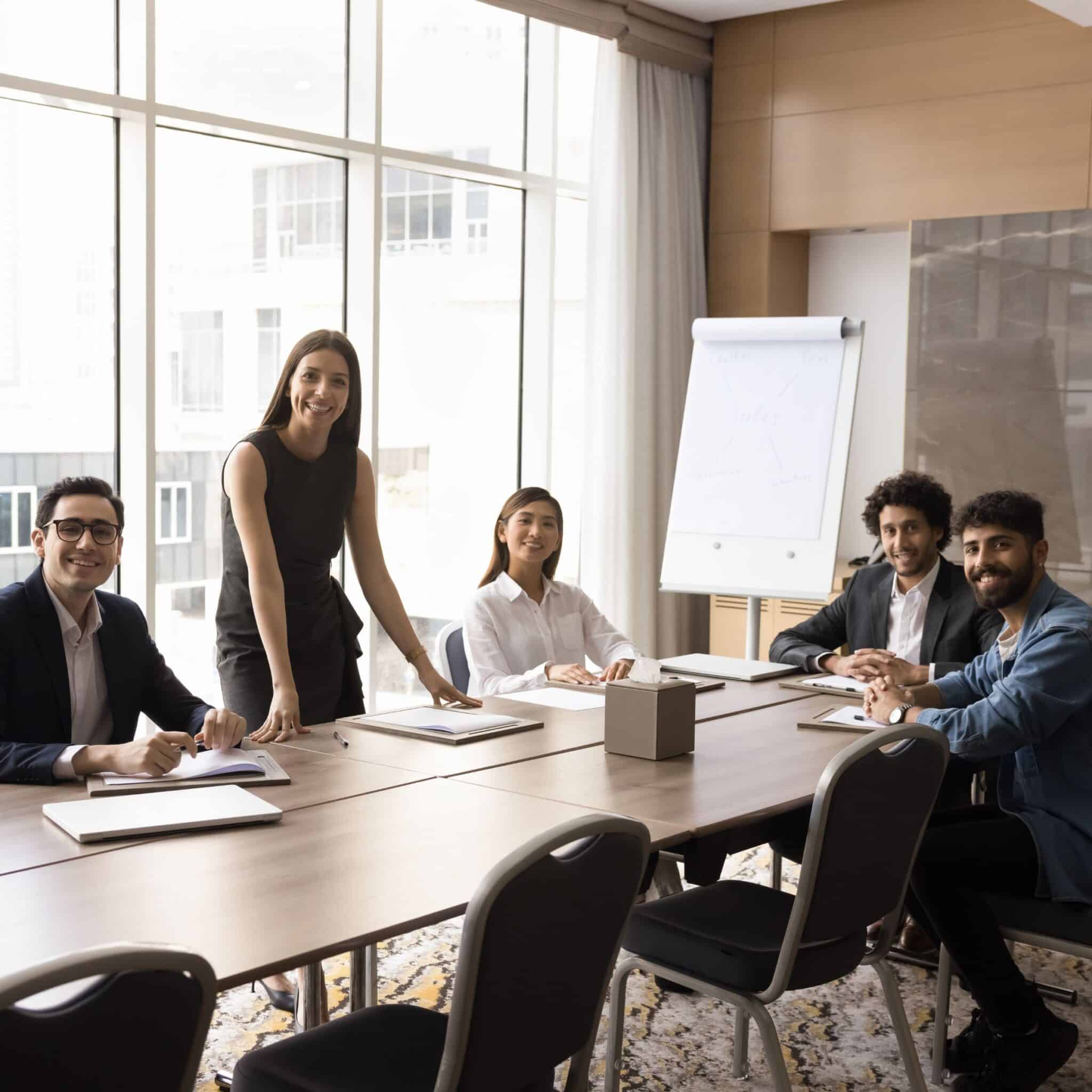 Group of professionals sitting together in a modern meeting room, smiling and discussing work around a conference table