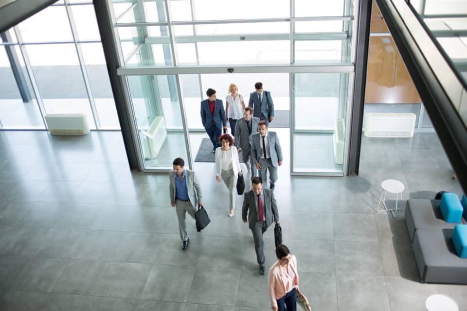 Group of people walking in and out of a main entrance in an office block.