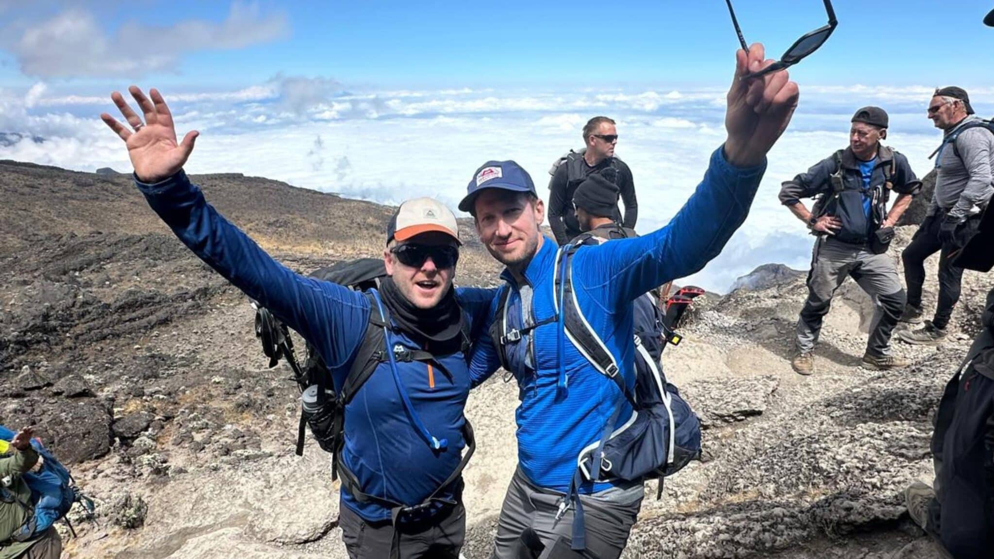 Group of hikers celebrating on a mountain trail above the clouds.