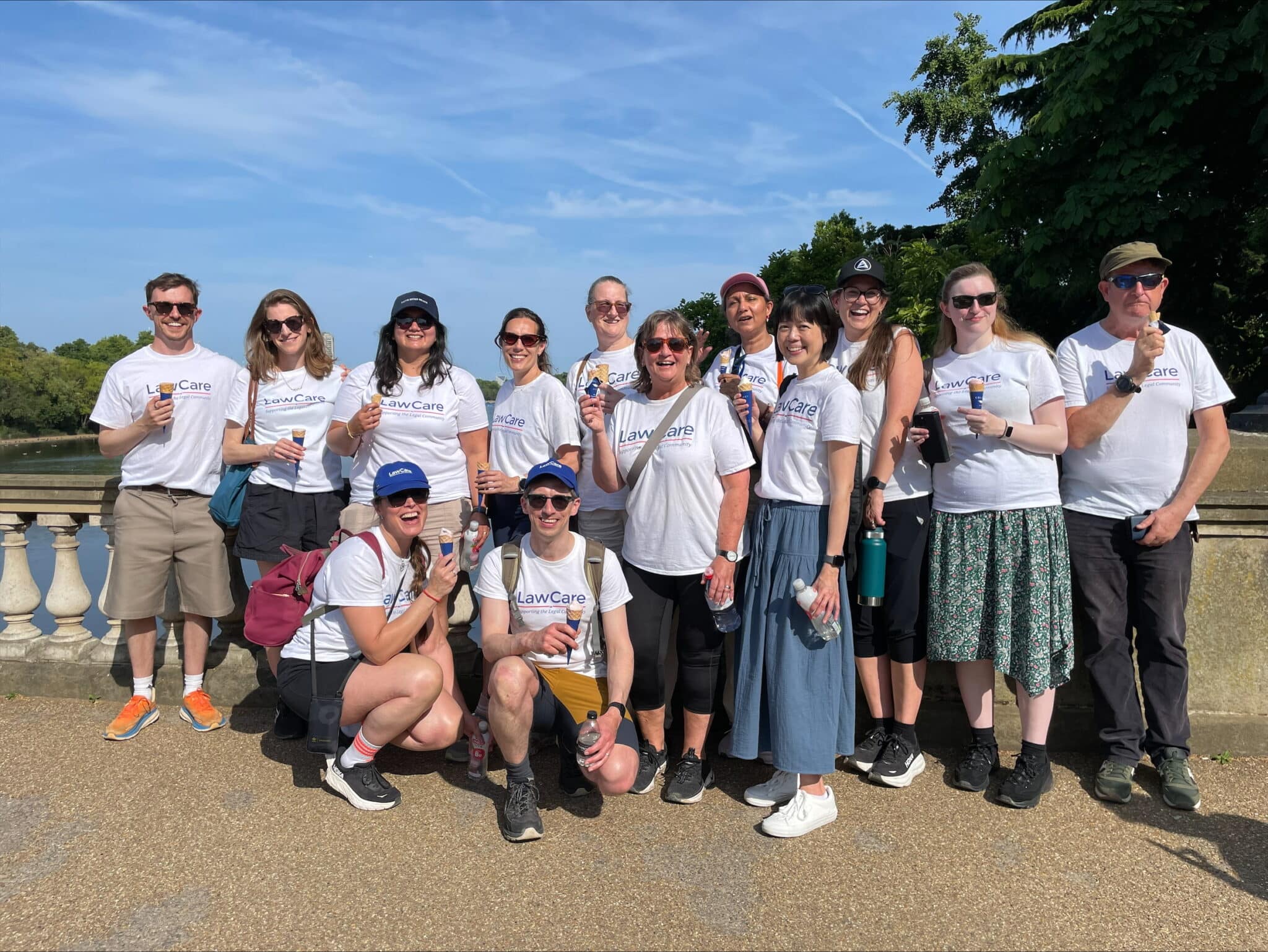 Group of people wearing matching LawCare T-shirts, smiling and holding ice creams, gathered outdoors on a sunny day during a charity walk.