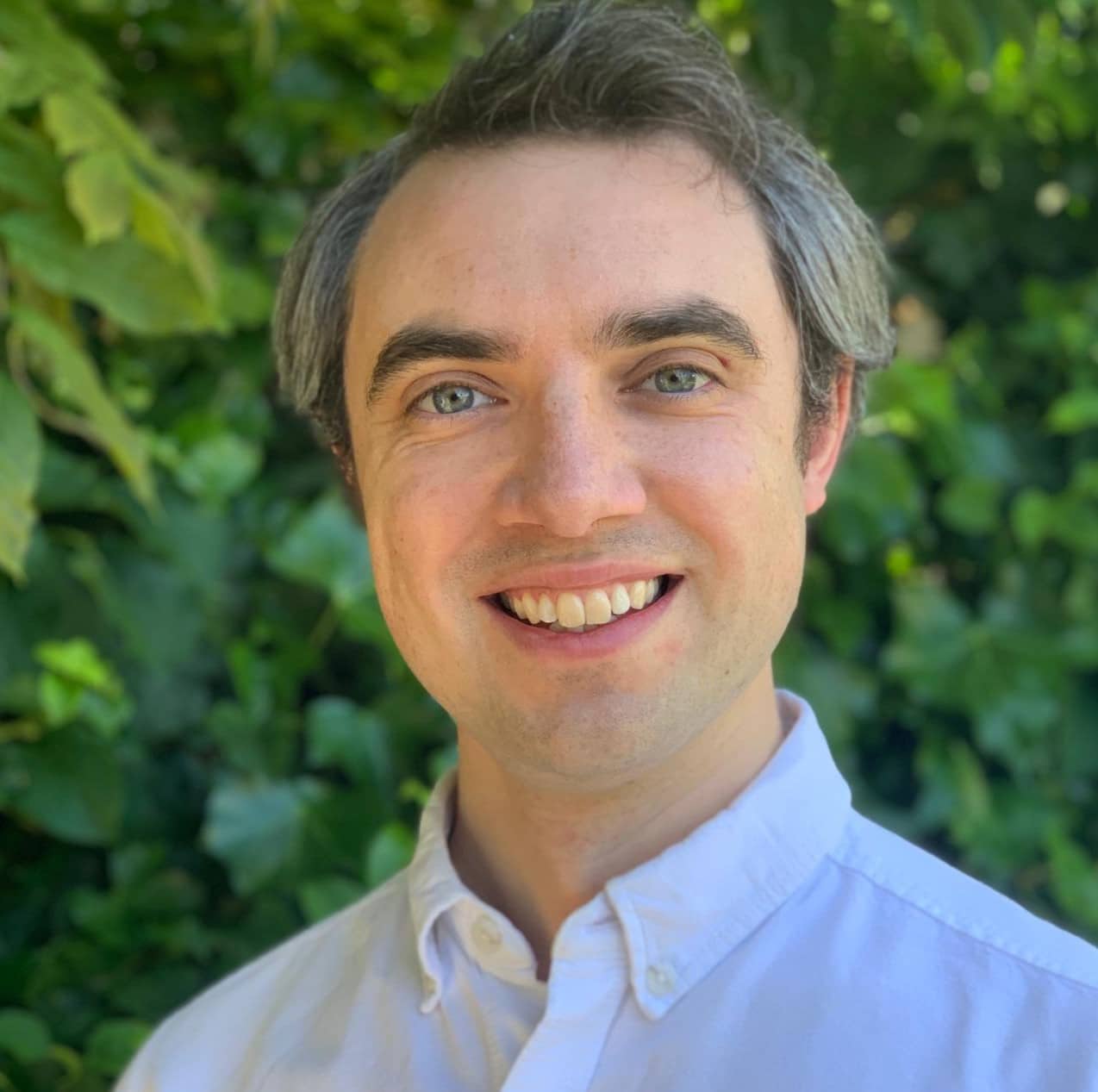 Man in shirt in front of green bush smiling