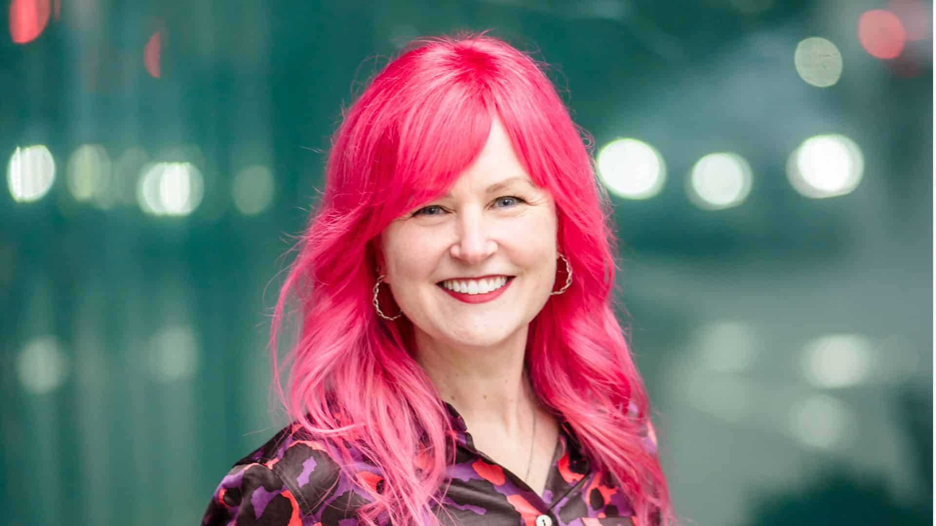 Woman with bright pink hair and pink leopard print blouse smiling at the camera