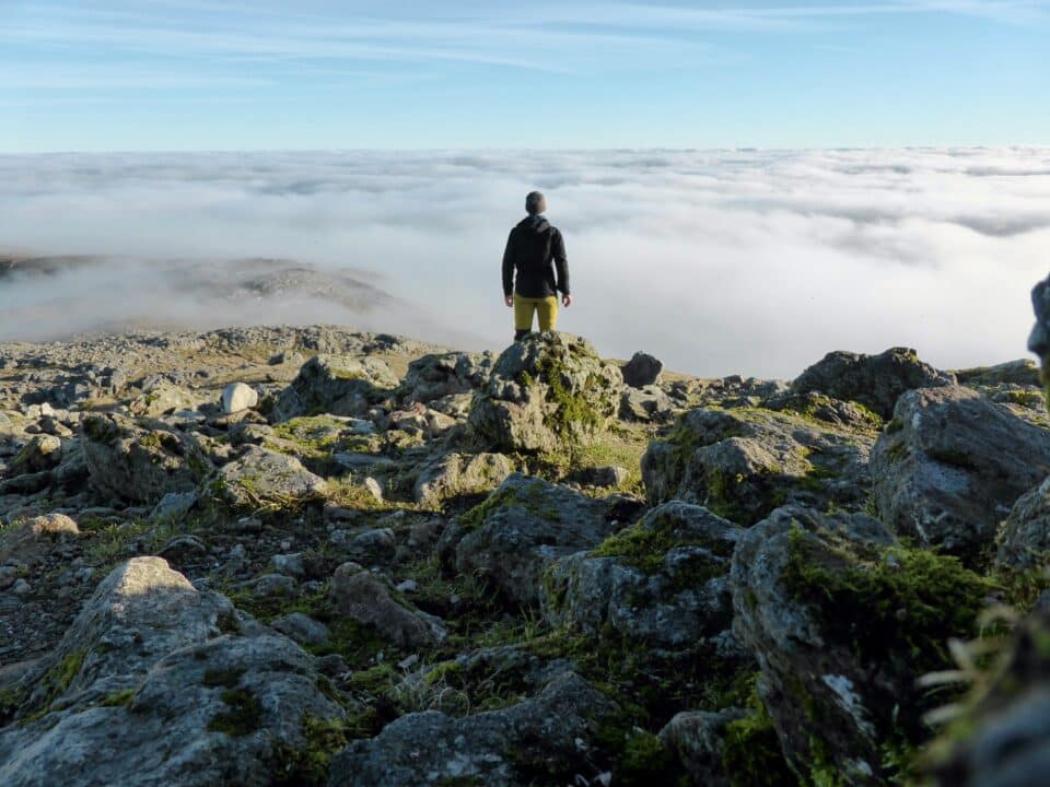 Man stood on hill facing away from the camera and looking out over some clouds