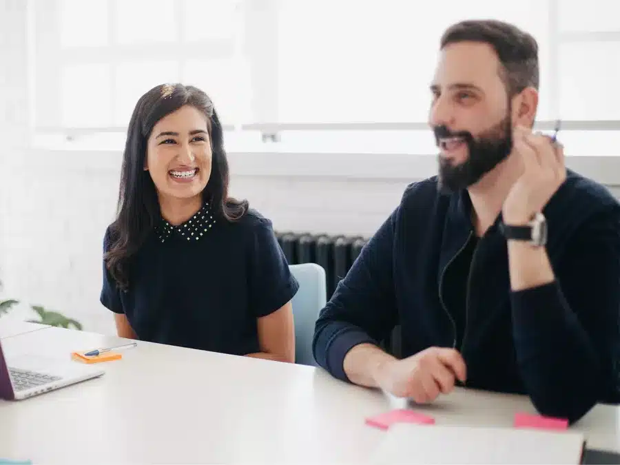 Man and woman sat at desk with laptop smiling and looking happy
