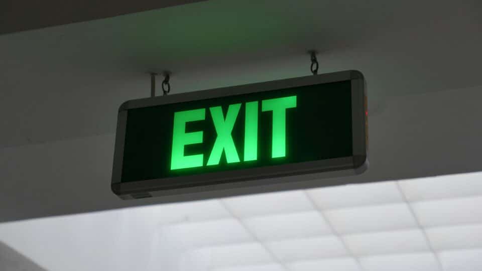 Green neon exit sign hanging high up against a wall