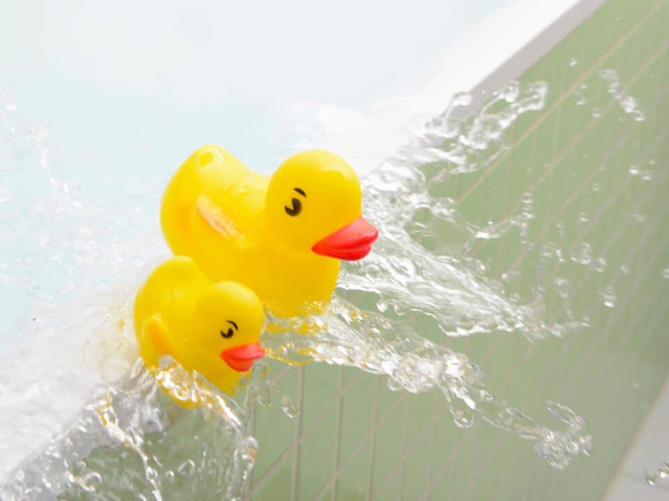 Two yellow rubber ducks tipping over the edge of an overflowing bath.