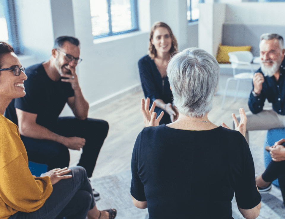 Group of people sitting in a circle, talking and smiling during a peer support session