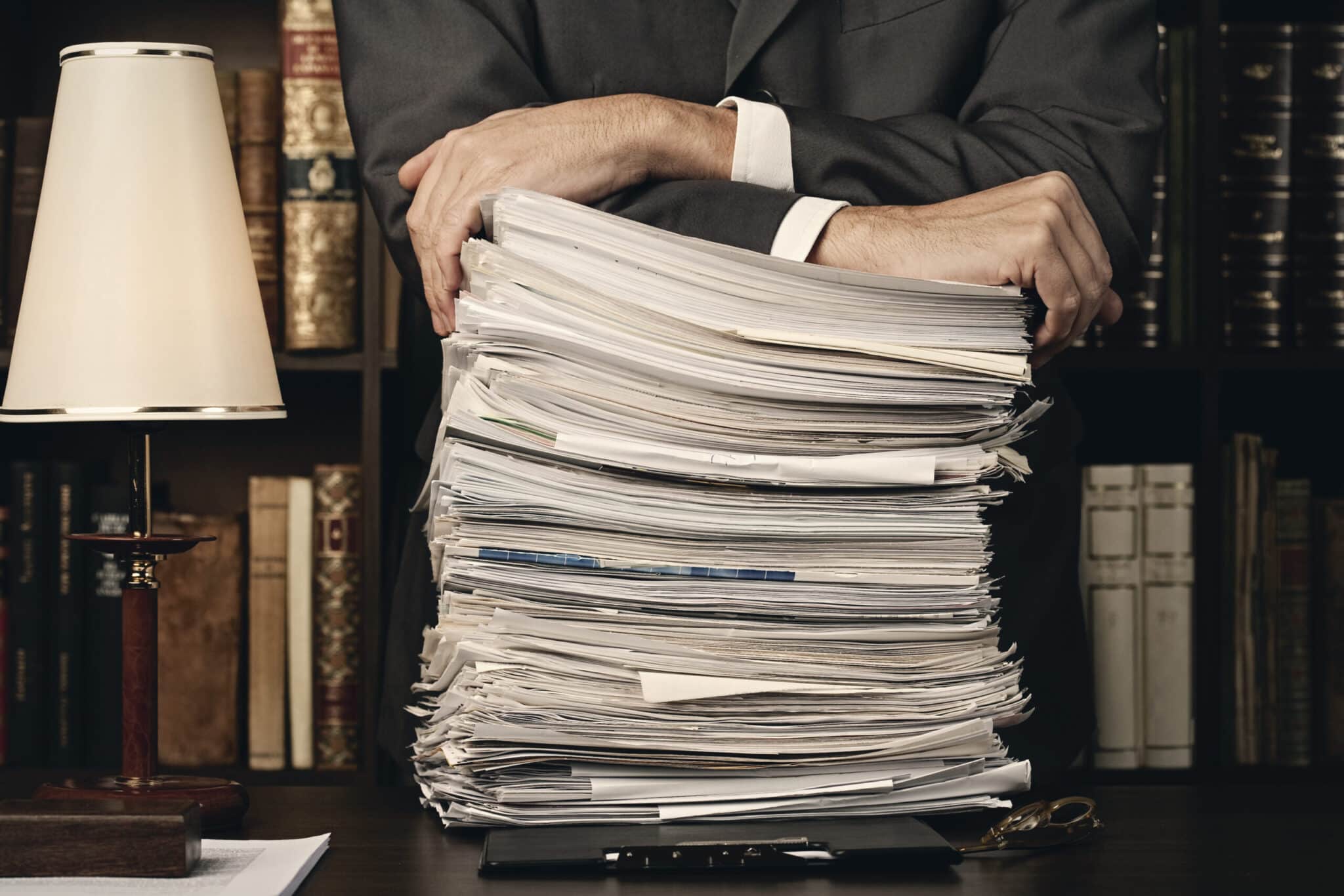 Man in suit in an office leaning on a huge pile of paperwork