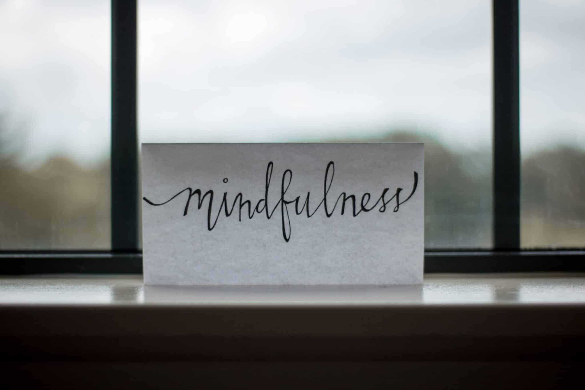 Card with the word ‘mindfulness’ written in calligraphy, placed on a windowsill.