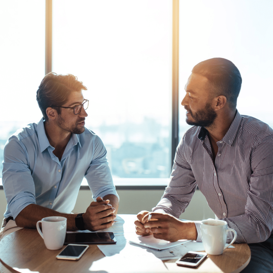 two men sat at a table talking to each other and looking relaxed