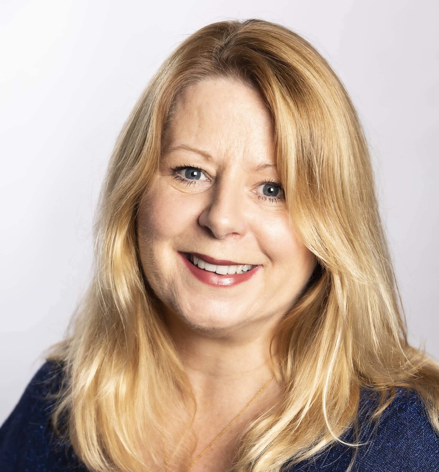 Woman with long blonde hair wearing a navy top and a necklace.