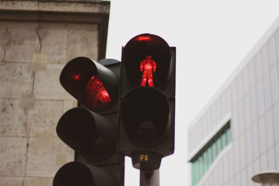 Close-up of a red traffic light and pedestrian signal against a city building background, indicating vehicles and people must stop.