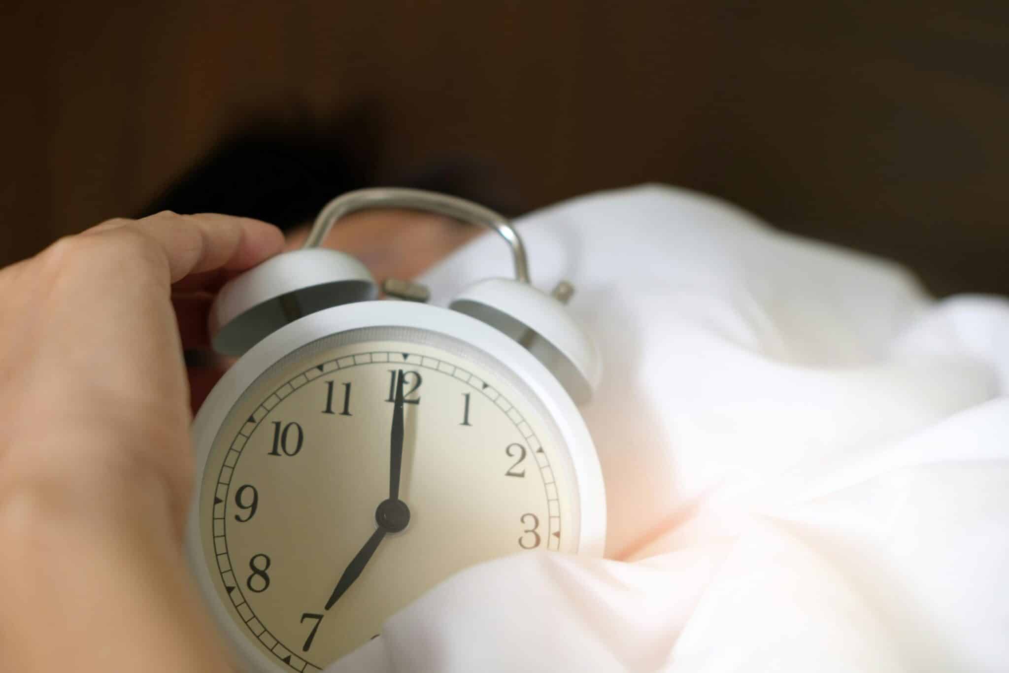 alarm clock lying on a bed under someone's arm
