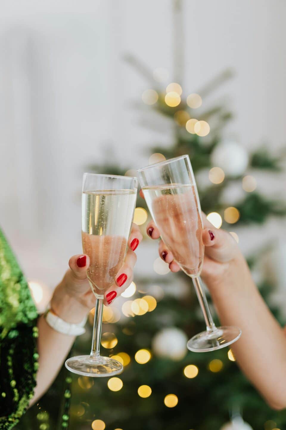 Two champagne flutes clinking together in front of a blurred out Christmas tree