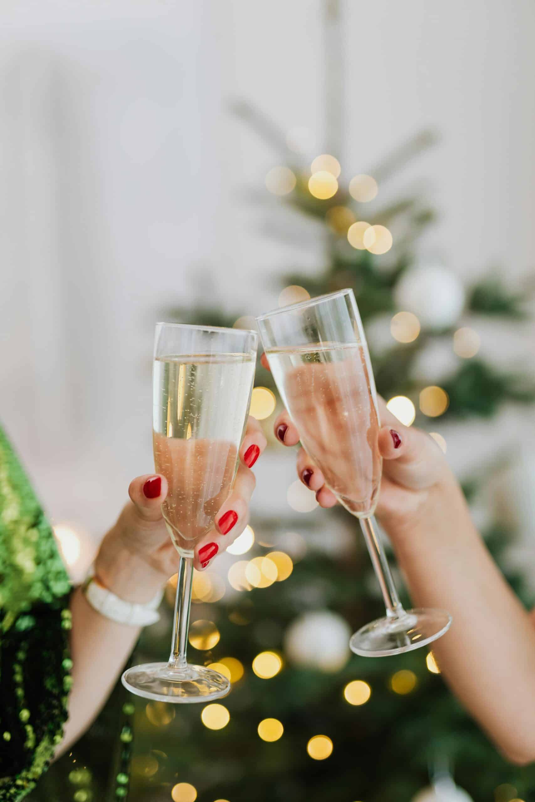 Two champagne flutes clinking together in front of a blurred out Christmas tree