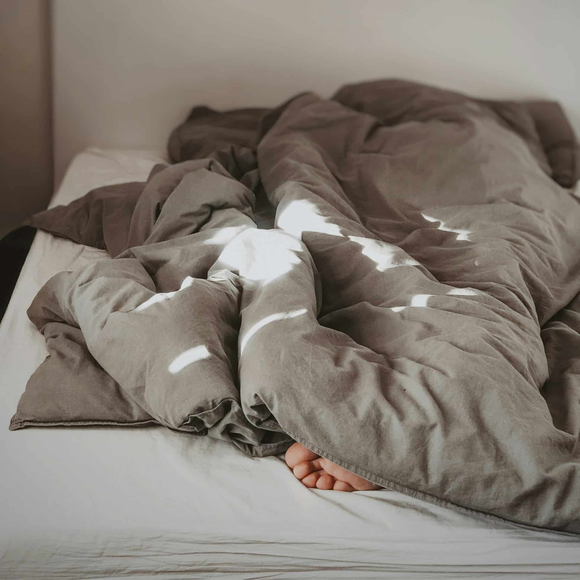 Person wrapped up in a duvet in bed with only their toes peeping out.