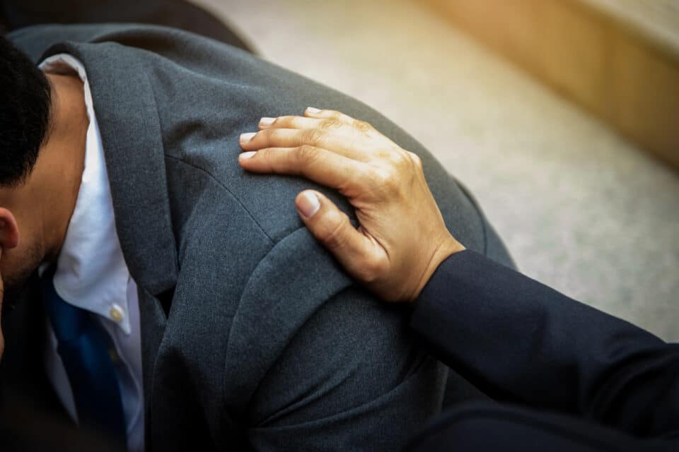 Close-up of a hand placed on a person’s shoulder, offering comfort and support