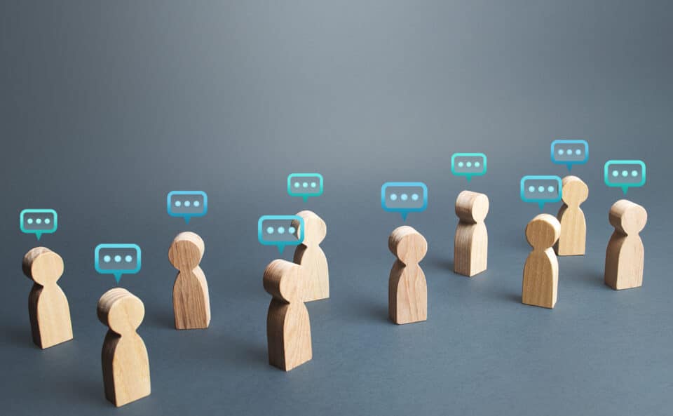 Wooden human figures with speech bubble icons above them, symbolising communication and discussion.