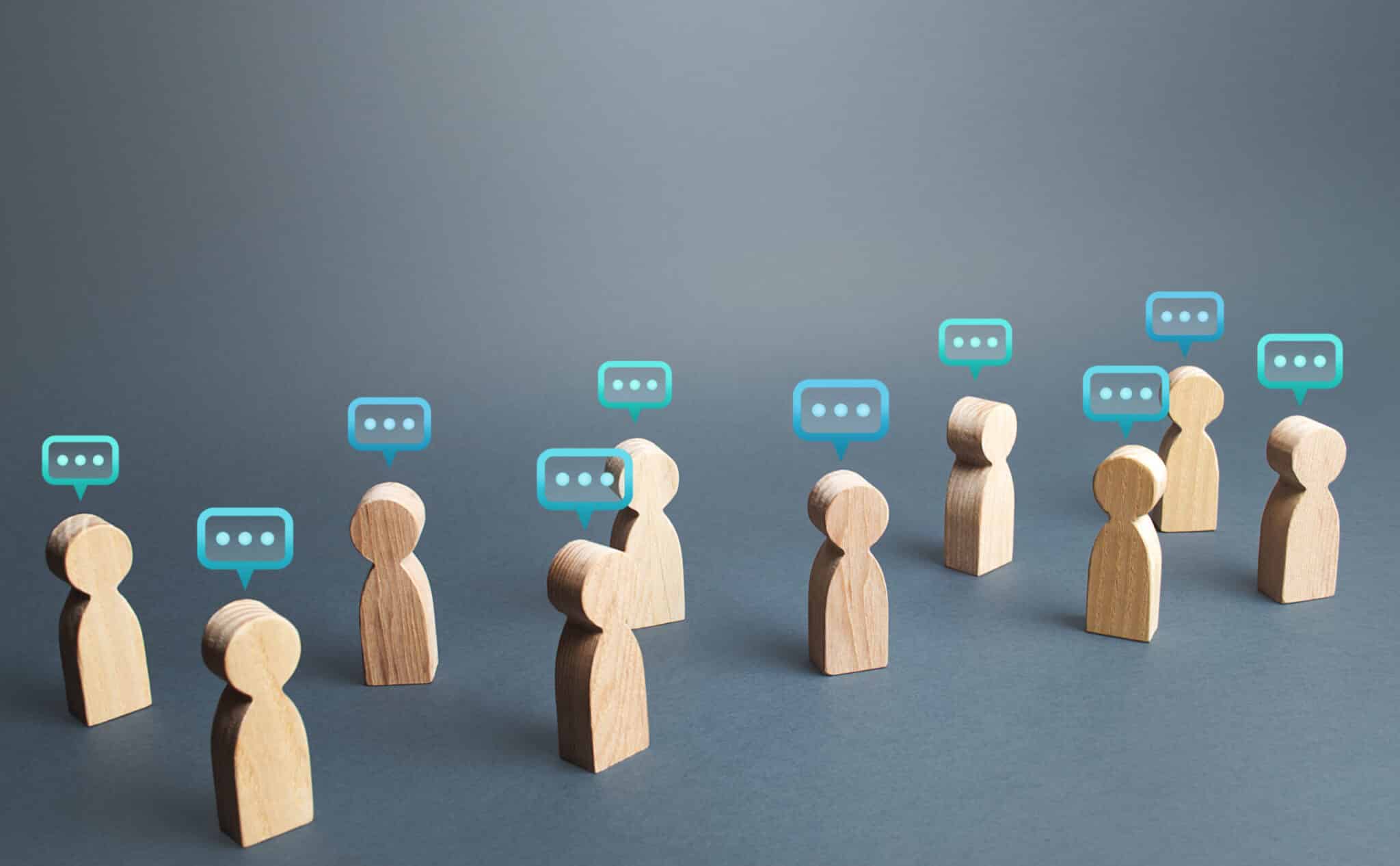 Wooden human figures with speech bubble icons above them, symbolising communication and discussion.