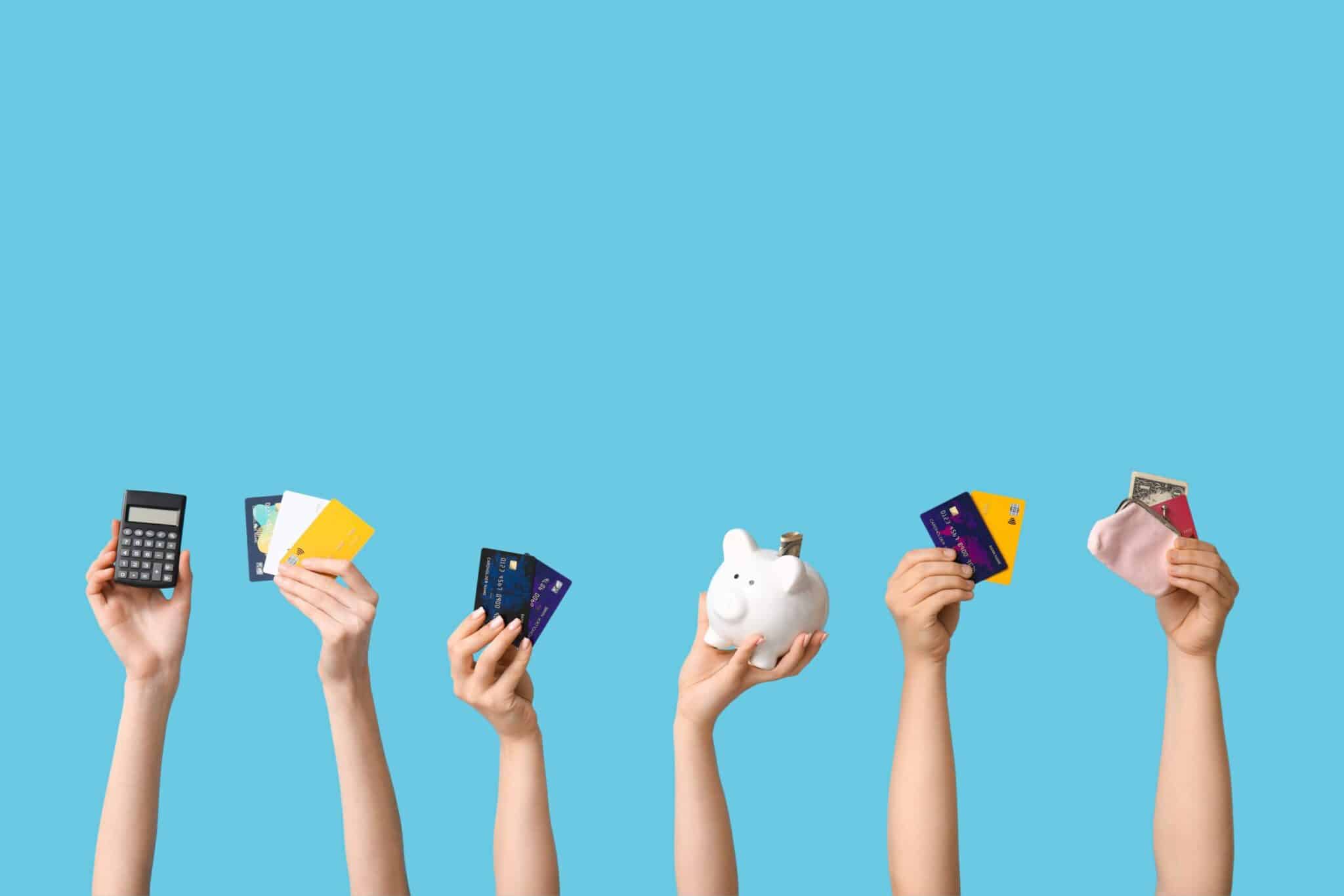 Multiple hands holding up a calculator, credit cards, a piggy bank, and a coin purse against a blue background, symbolizing personal finance and money management.