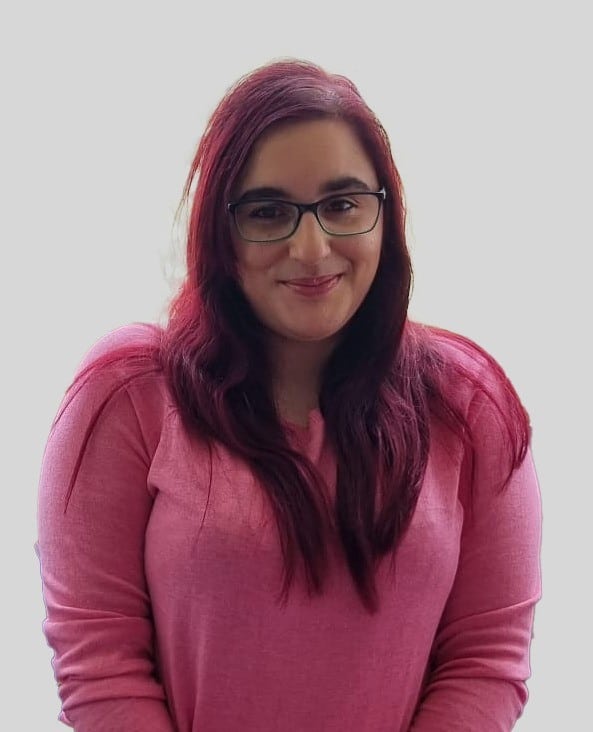 Young woman with long dark hair and glasses. wearing a pink top.