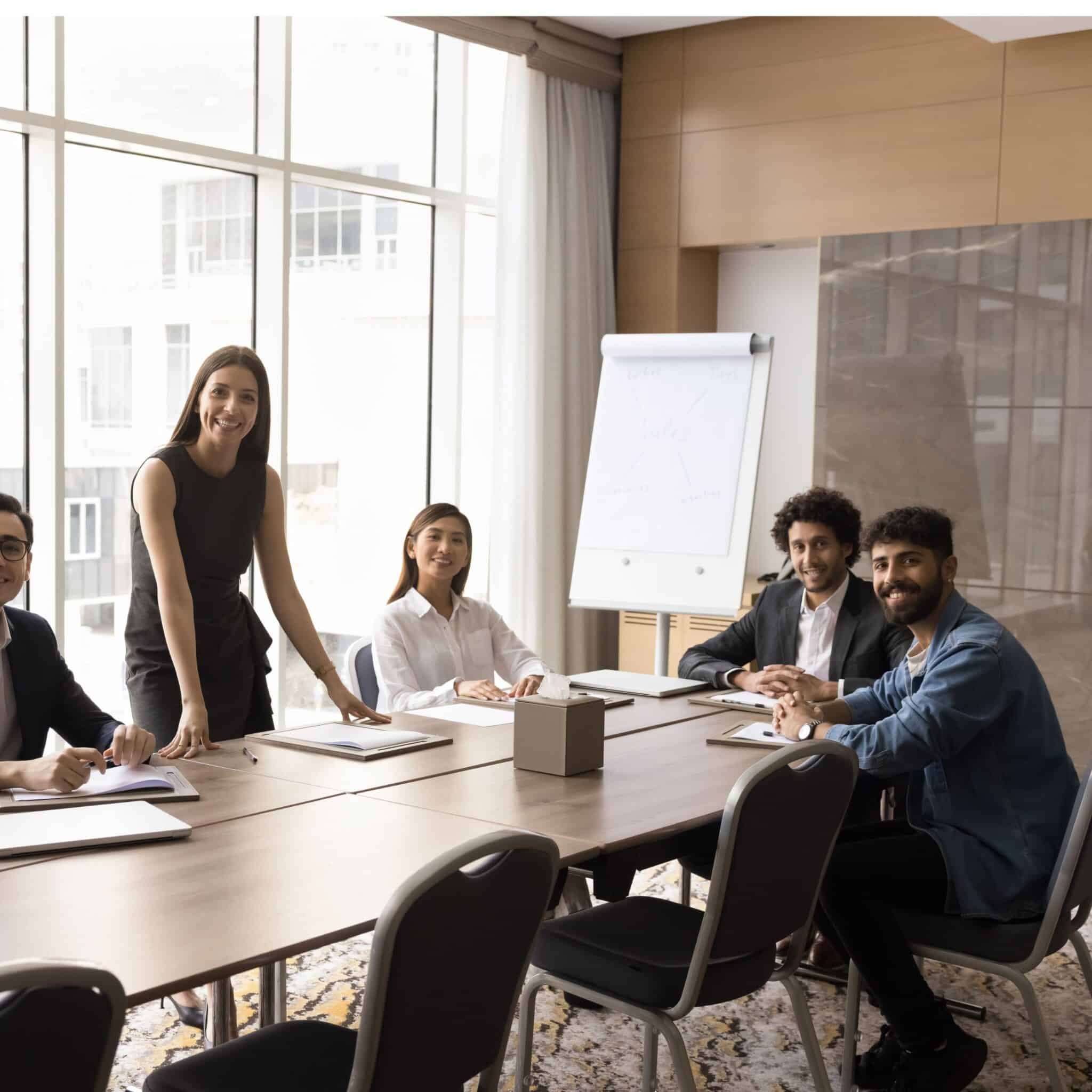Group of professionals sitting together in a modern meeting room, smiling and discussing work around a conference table