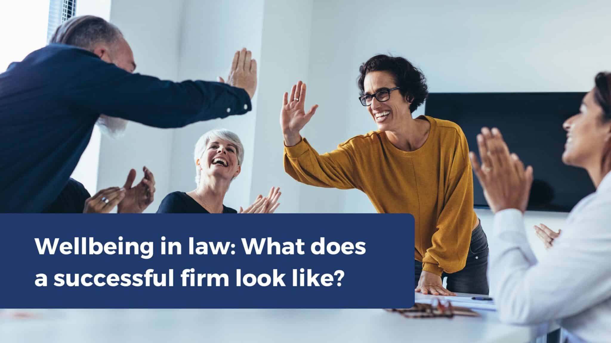 "Group of colleagues smiling, high-fiving, and clapping in a meeting room, with text reading ‘Wellbeing in law: What does a successful firm look like?