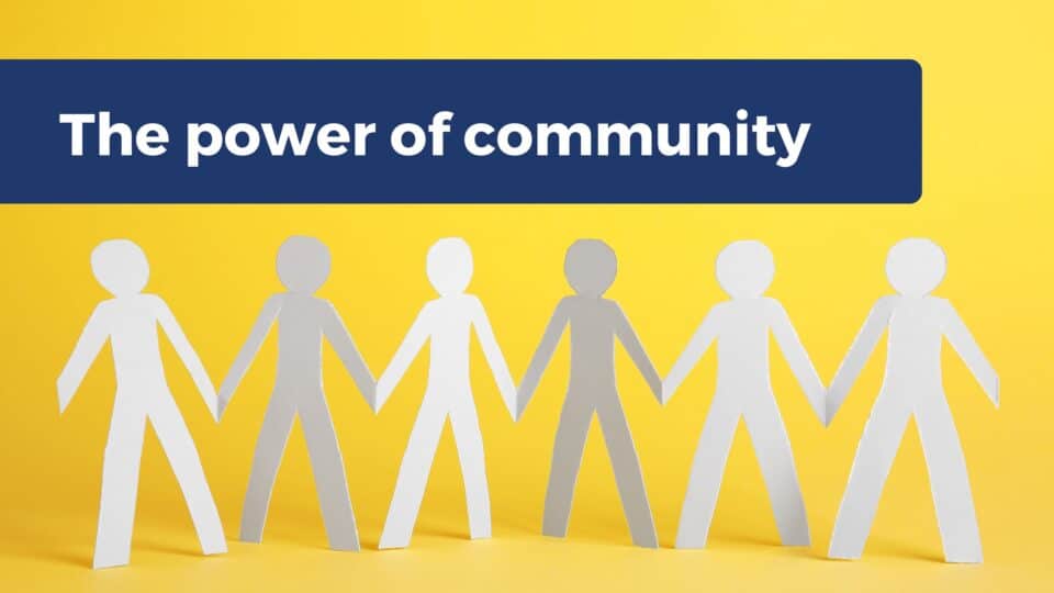 Paper cut-out figures holding hands in a row against a yellow background, with the text 'The power of community' above them