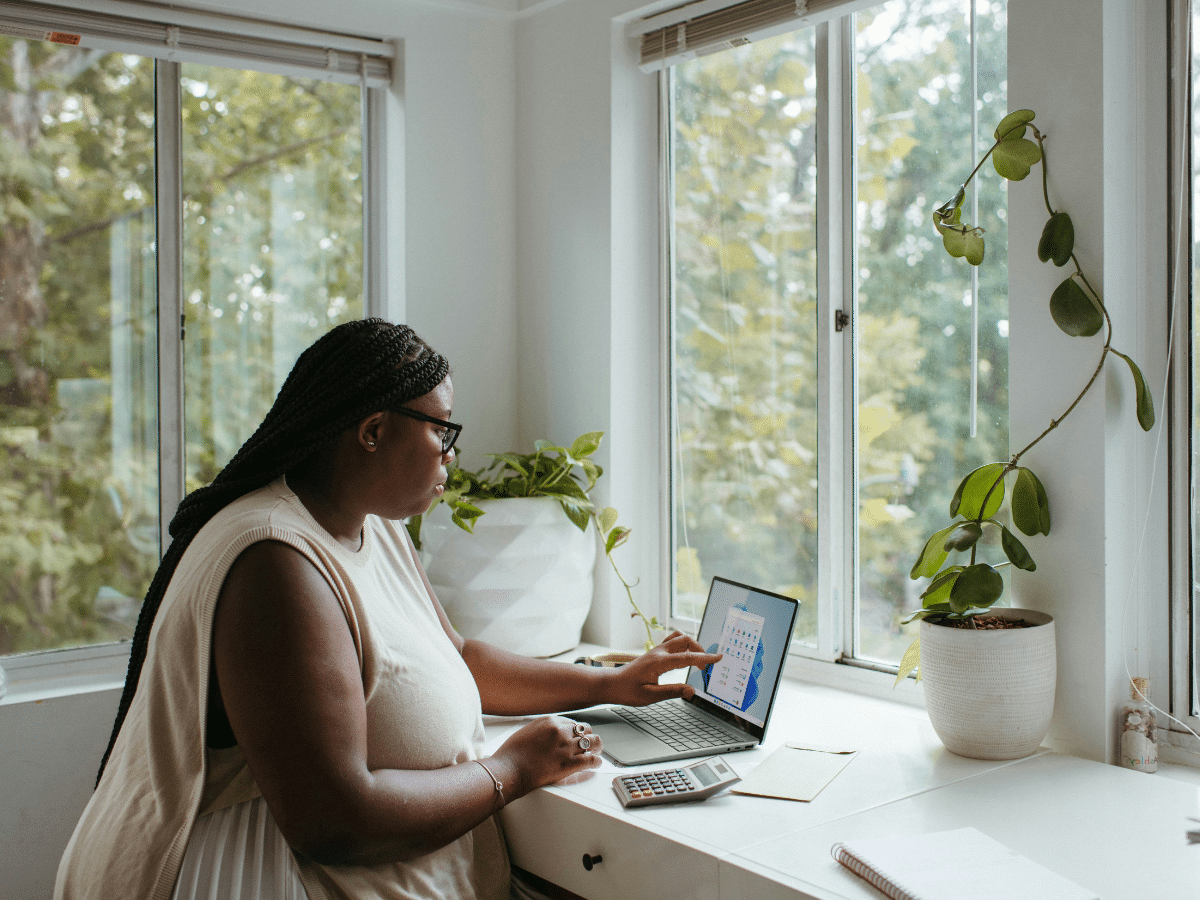 young woman sat in front of a window at home working on a laptop