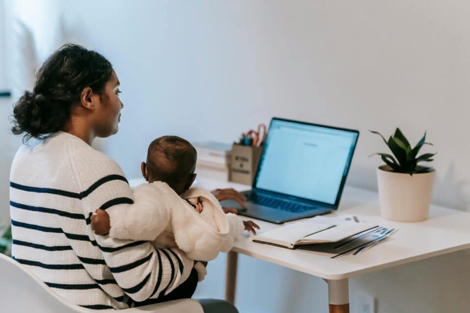 Woman sat at desk in front of a laptop and holding a young baby