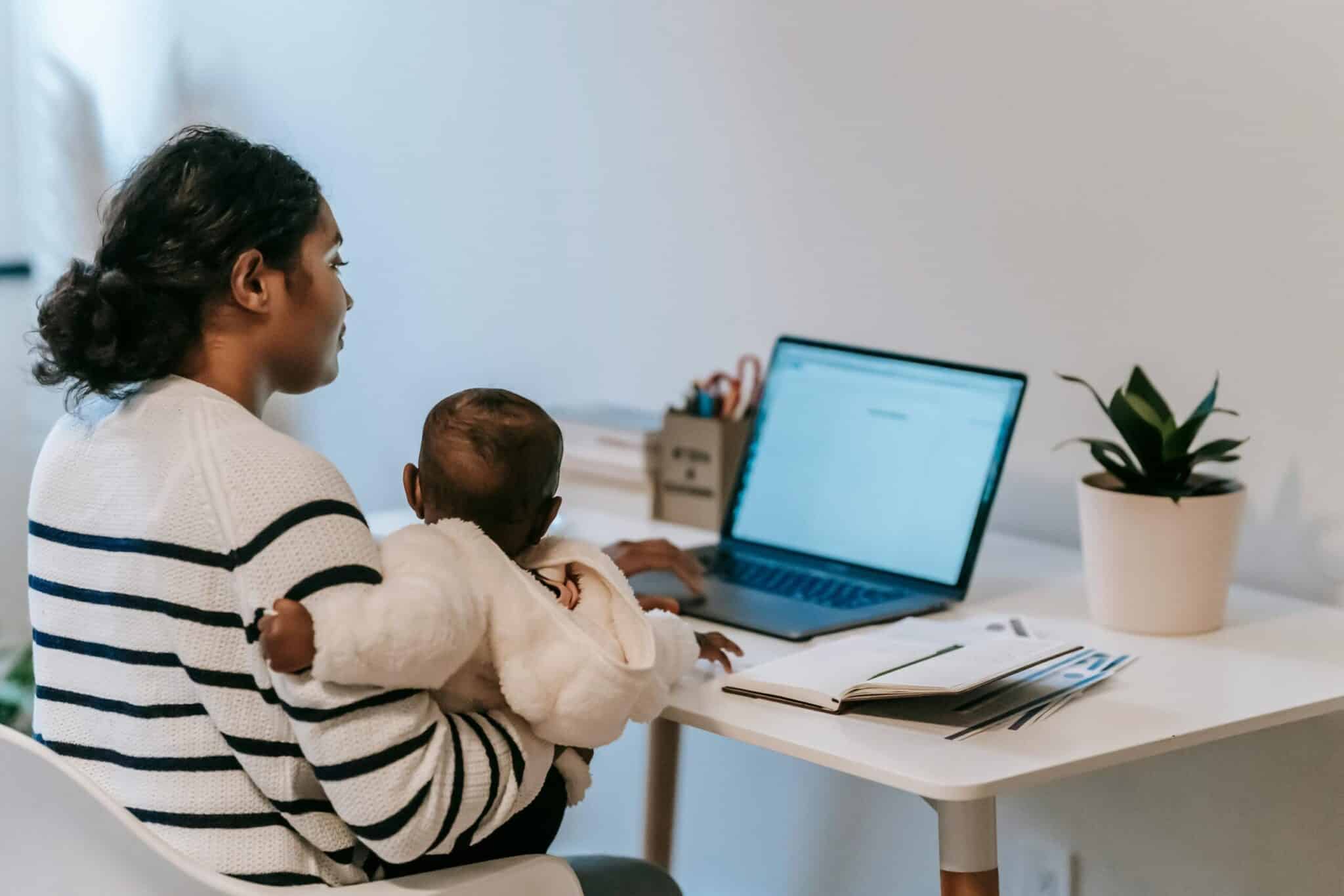 Woman sat at desk in front of a laptop and holding a young baby