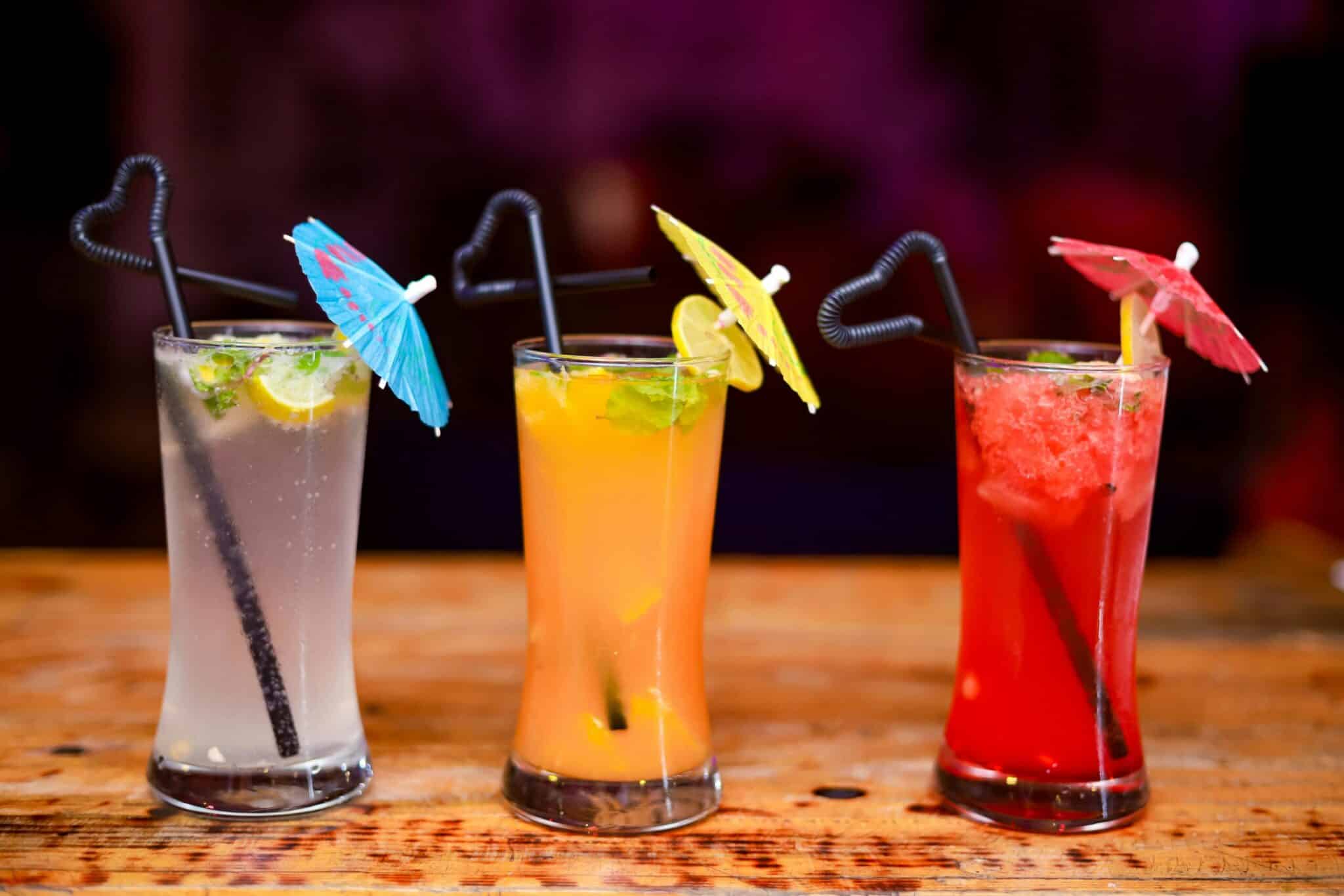 Three cocktail drinks in a row in tall glasses with paper umbrellas