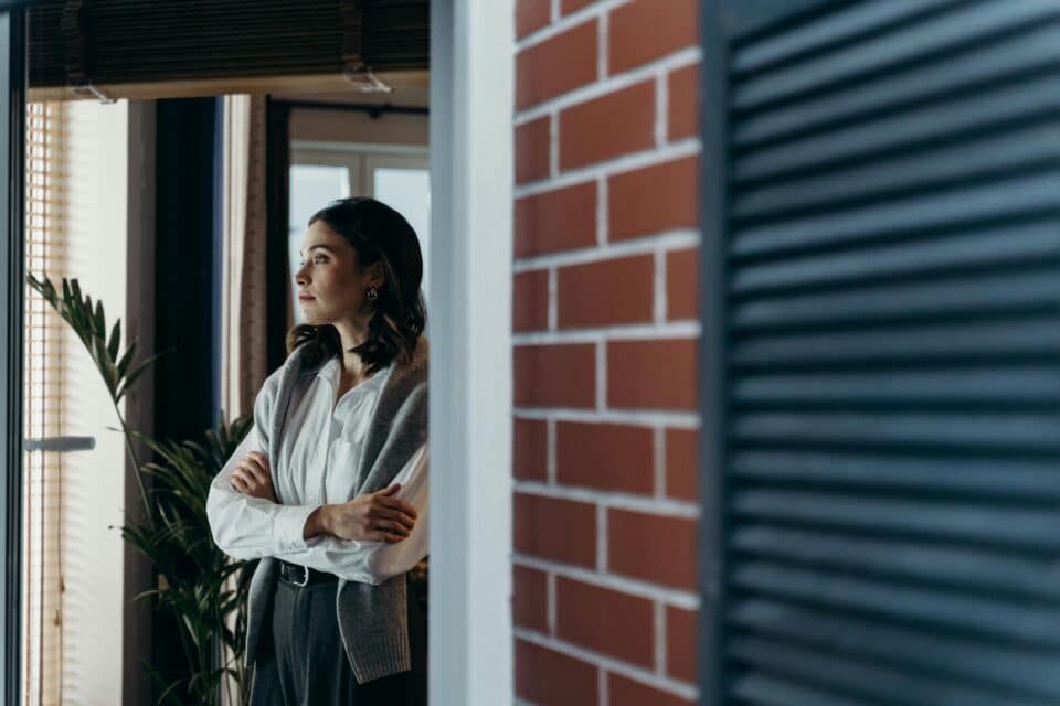 Person standing by a window with folded arms, looking thoughtful
