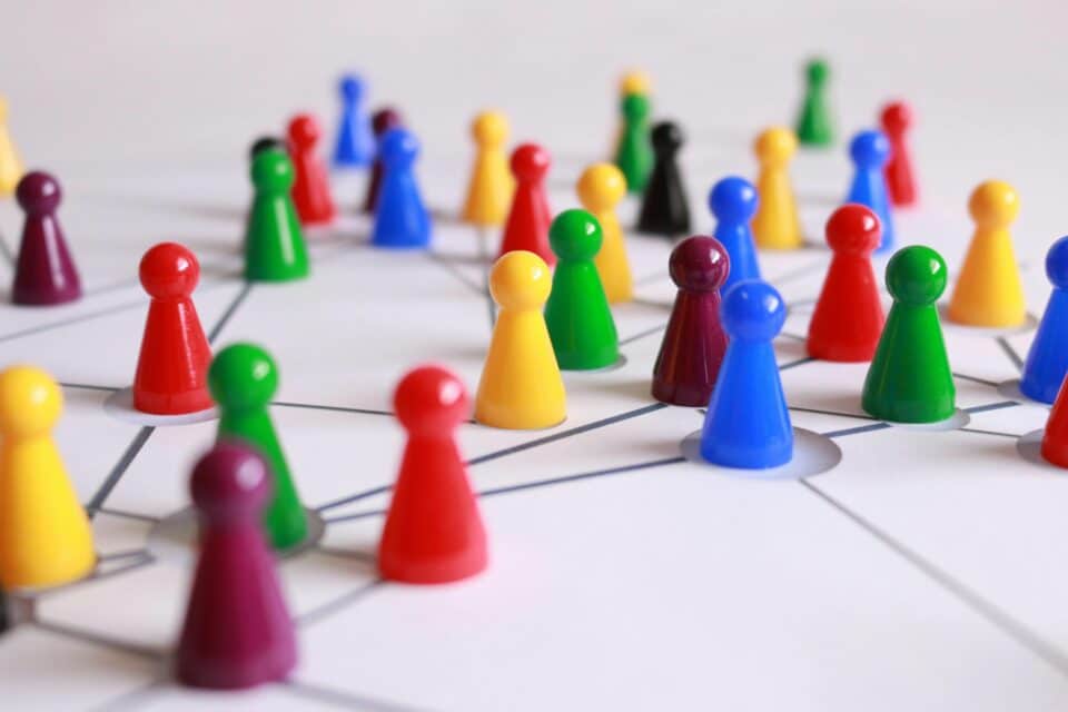Close-up of colourful game pieces connected by lines on a white surface, representing people in a network or community.