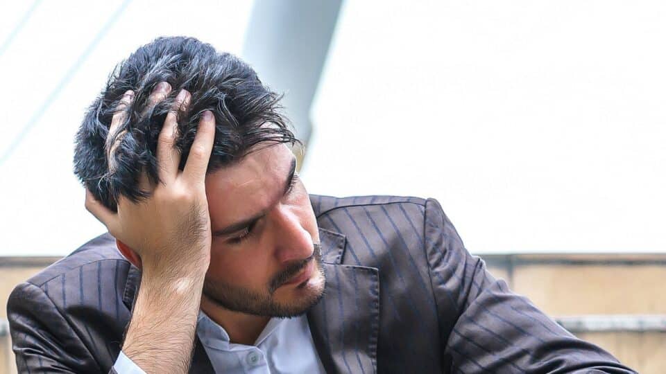 Man in a suit sitting on outdoor steps, looking distressed with his head in his hand.