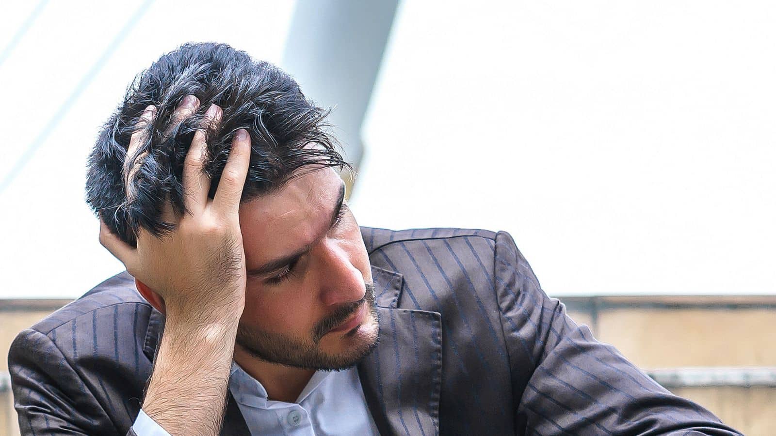 Man in a suit sitting on outdoor steps, looking distressed with his head in his hand.