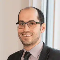 Young man with dark hair, glasses and wearing a suit and tie