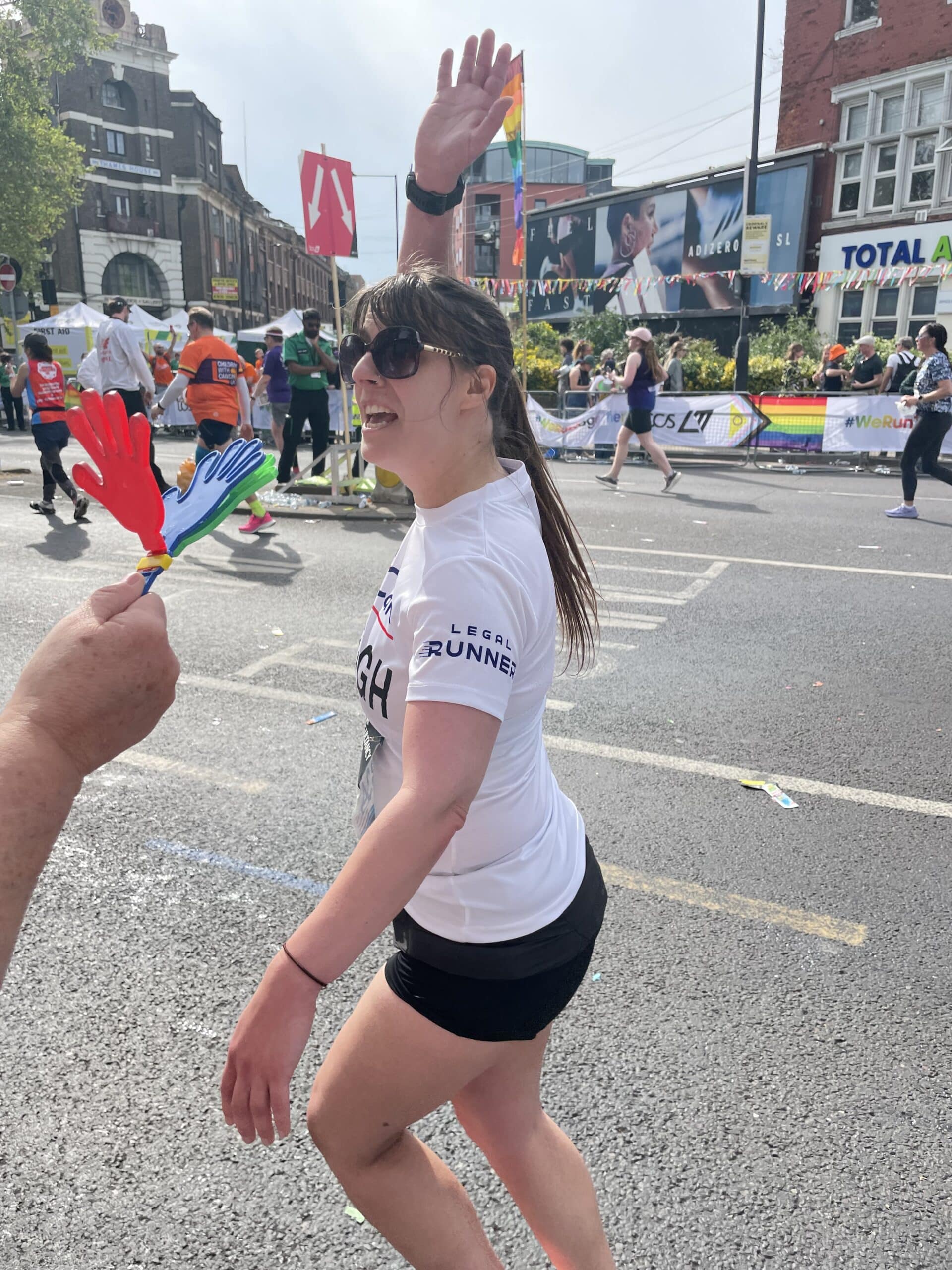 Kayleigh running past (mid race) and waving. She is wearing a LawCare t-shirt.