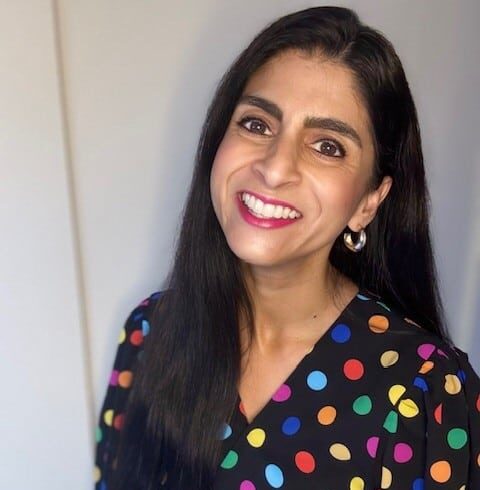 Young woman with long dark hair wearing a black top with multicoloured spots on it