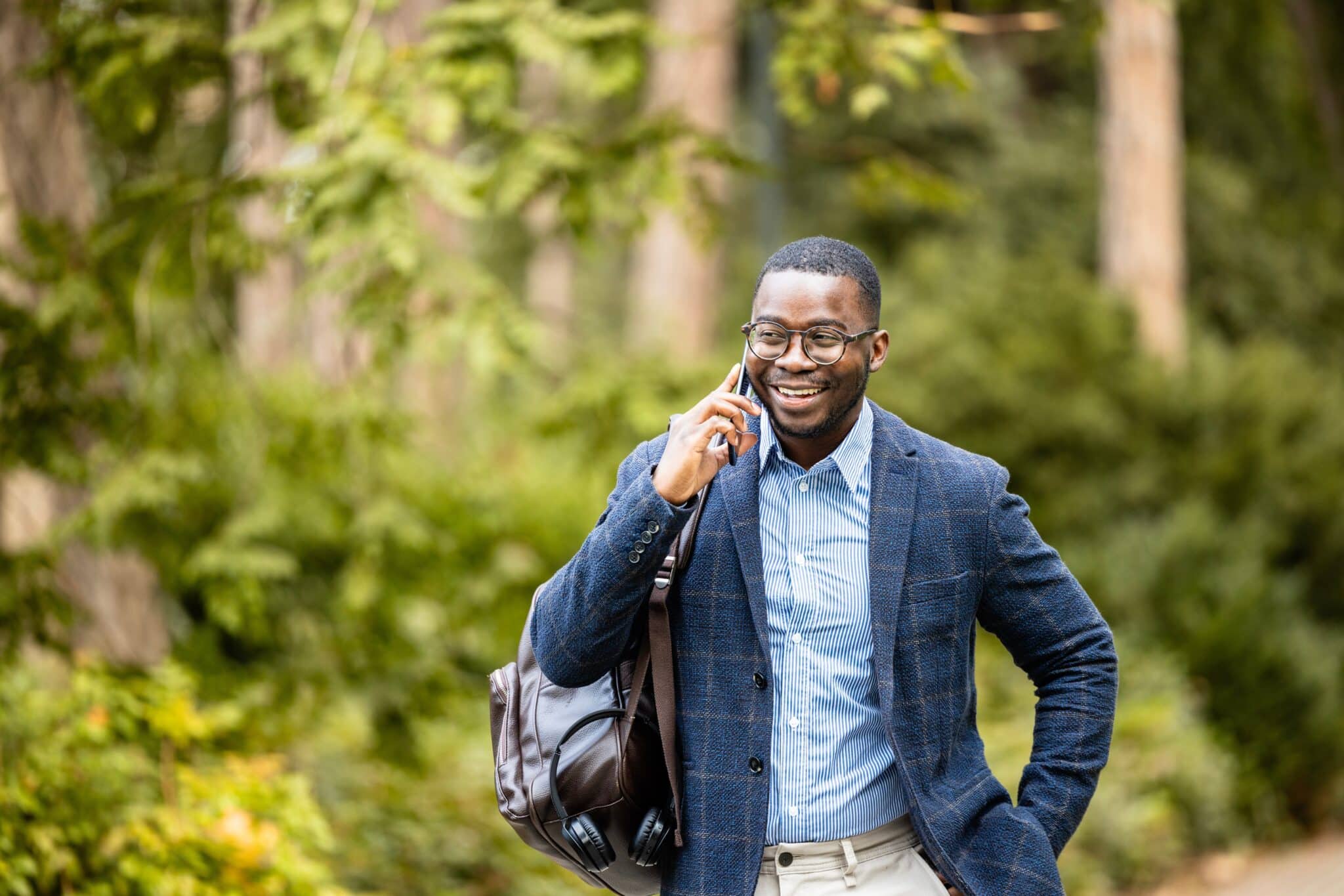 Smiling man with a shoulder bag talking on a mobile phone while walking outdoors.