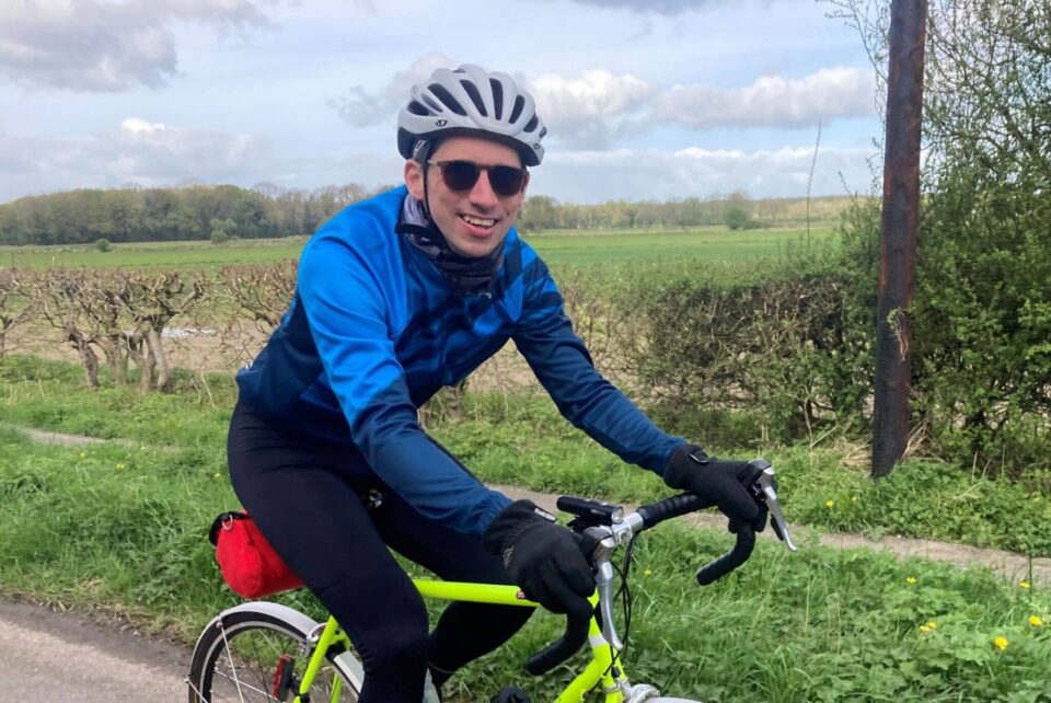 Smiling man on bike in the countryside in Yorkshire with green fields behind him.