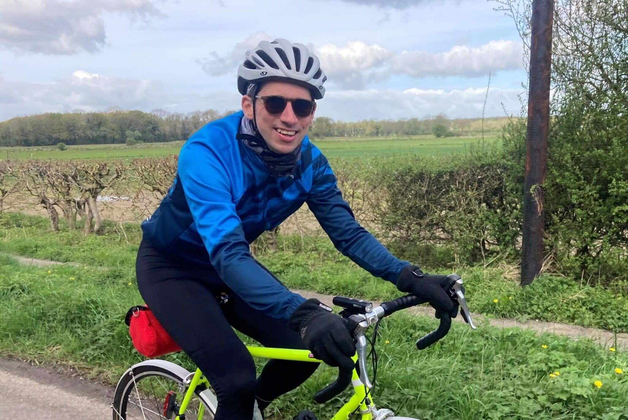 Smiling man on bike in the countryside in Yorkshire with green fields behind him.